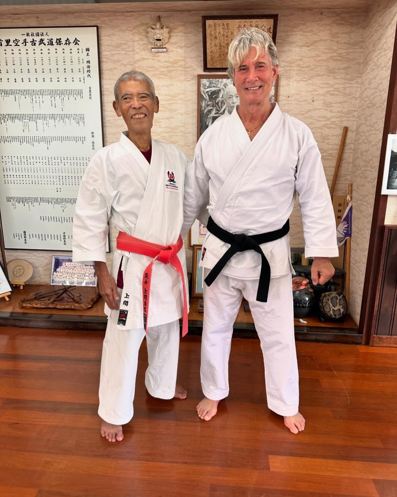 Richard Norton and a martial arts instructor pose together in a dojo, both wearing traditional white gi uniforms.