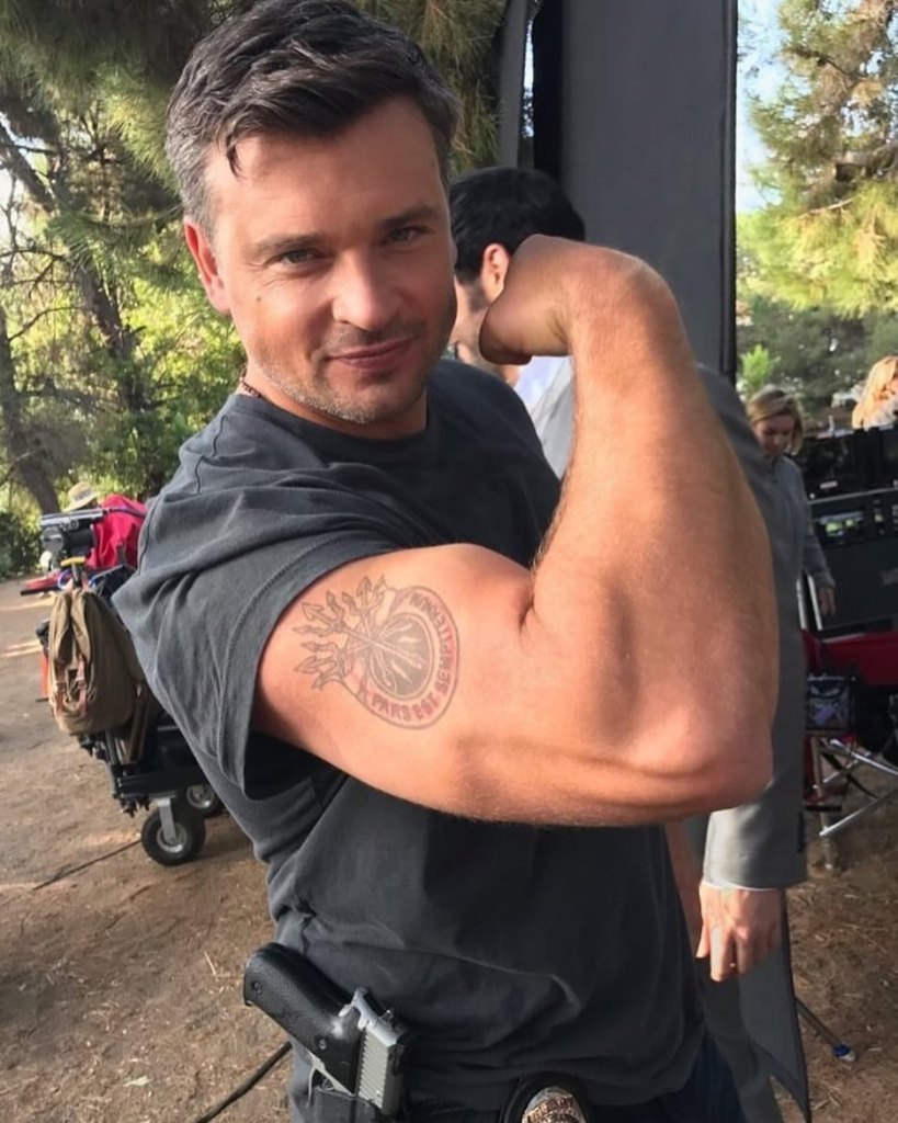 Tom Welling flexes his bicep to show off a tattoo on his arm.