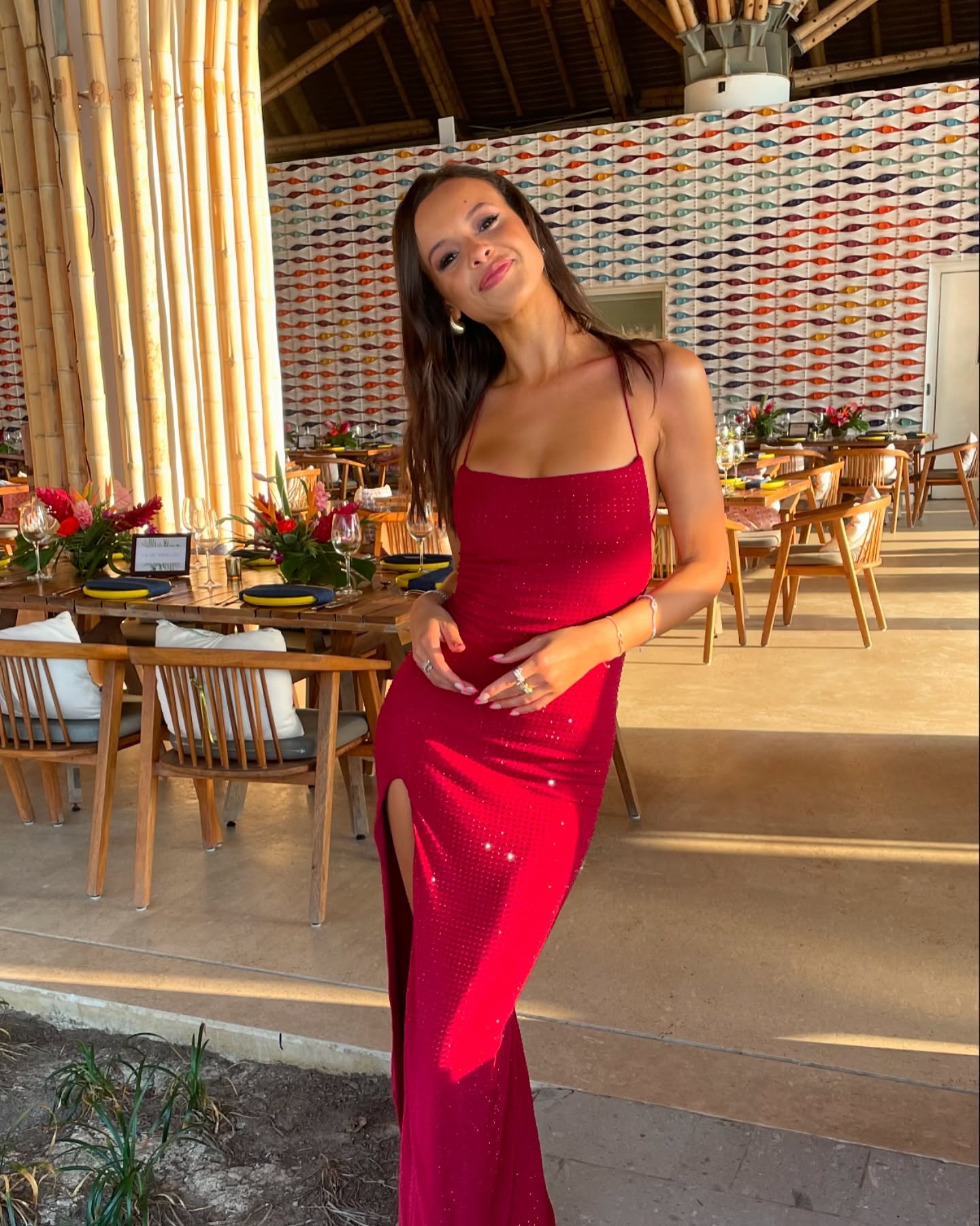 Aubrey Cleland wears a red spaghetti strap dress with a slit in an open-air restaurant.