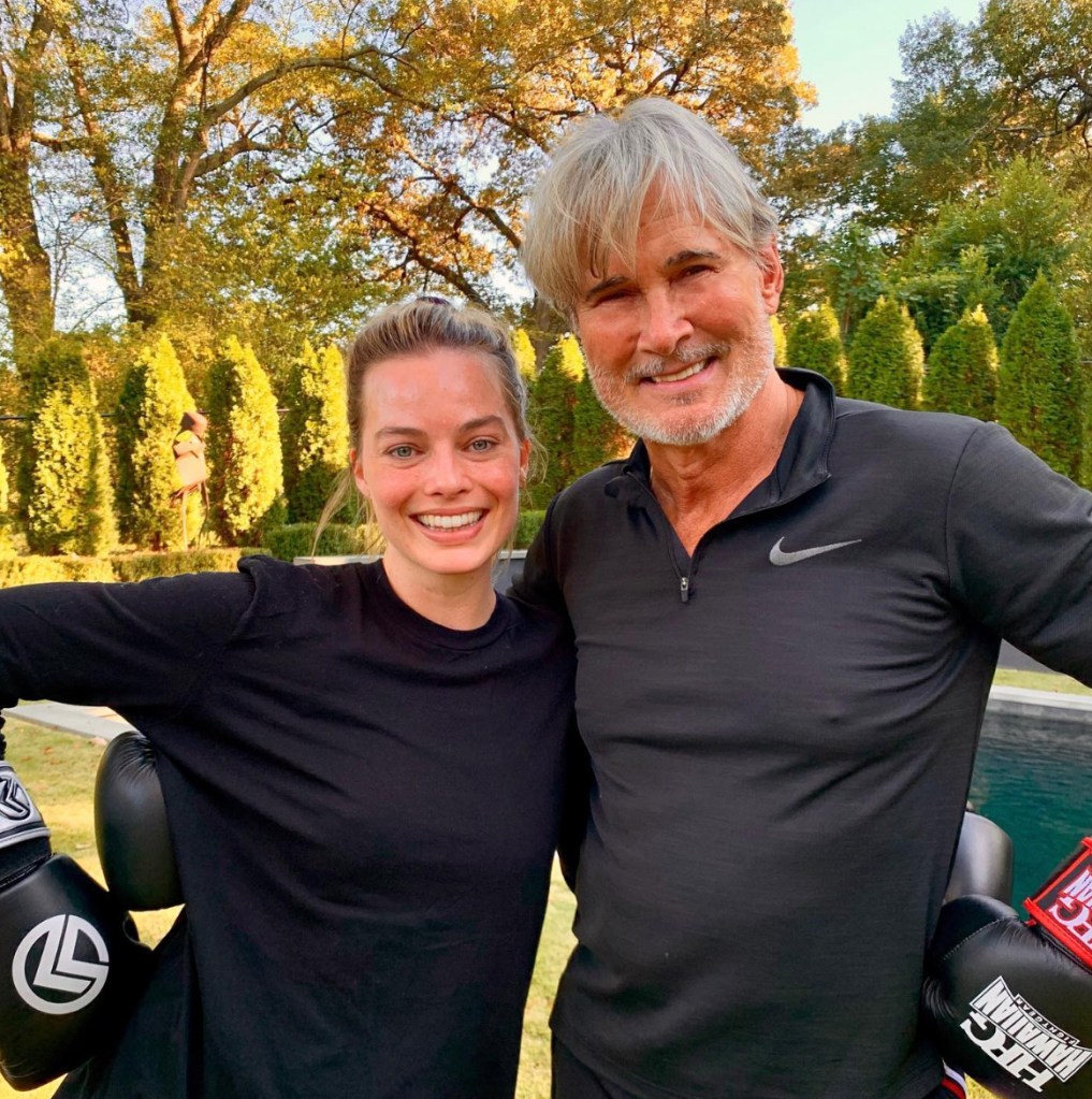 Richard Norton and Margot Robbie smiling outdoors while wearing black athletic clothes and boxing gloves.