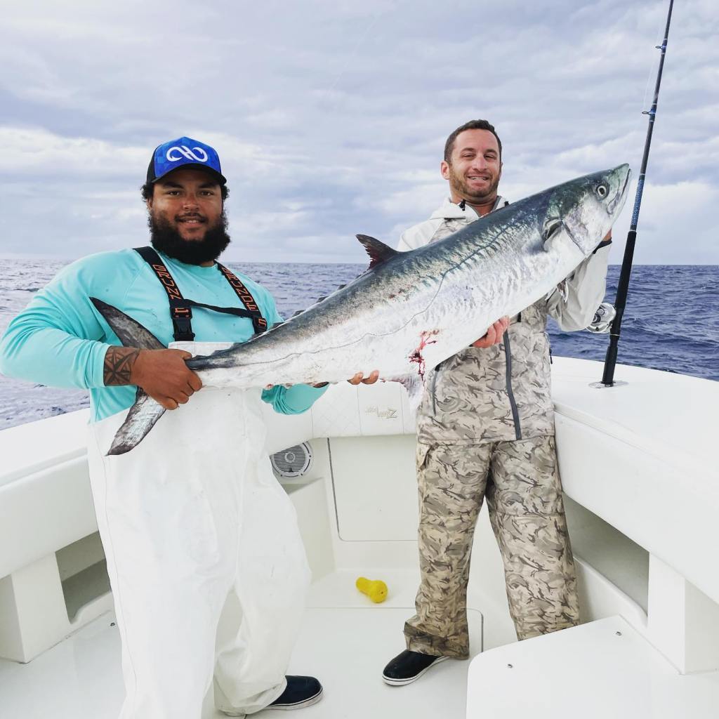 Two men holding a large fish on a boat.