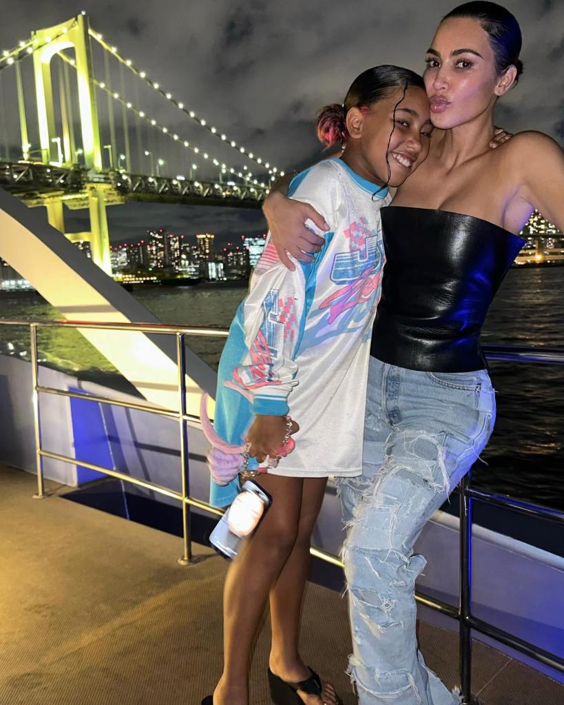 Kim Kardashian and North West hugging on a boat at night, with a lit bridge and city skyline in the background.