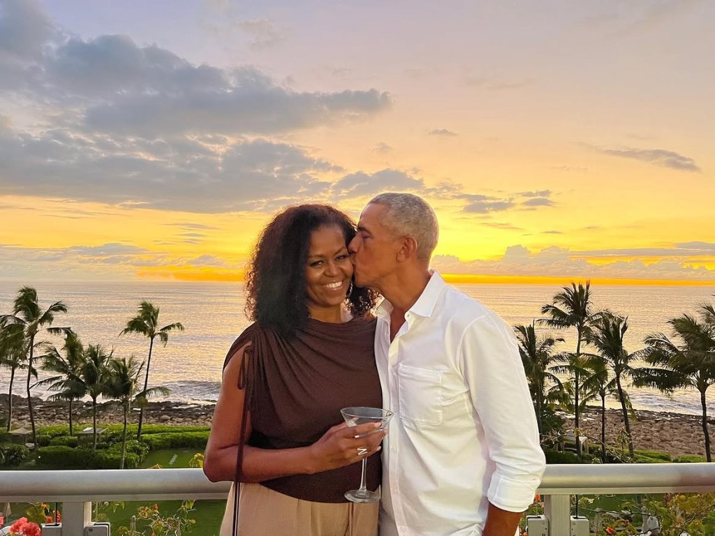 Barack Obama kissing Michelle Obama on the cheek with an ocean sunset in the background.