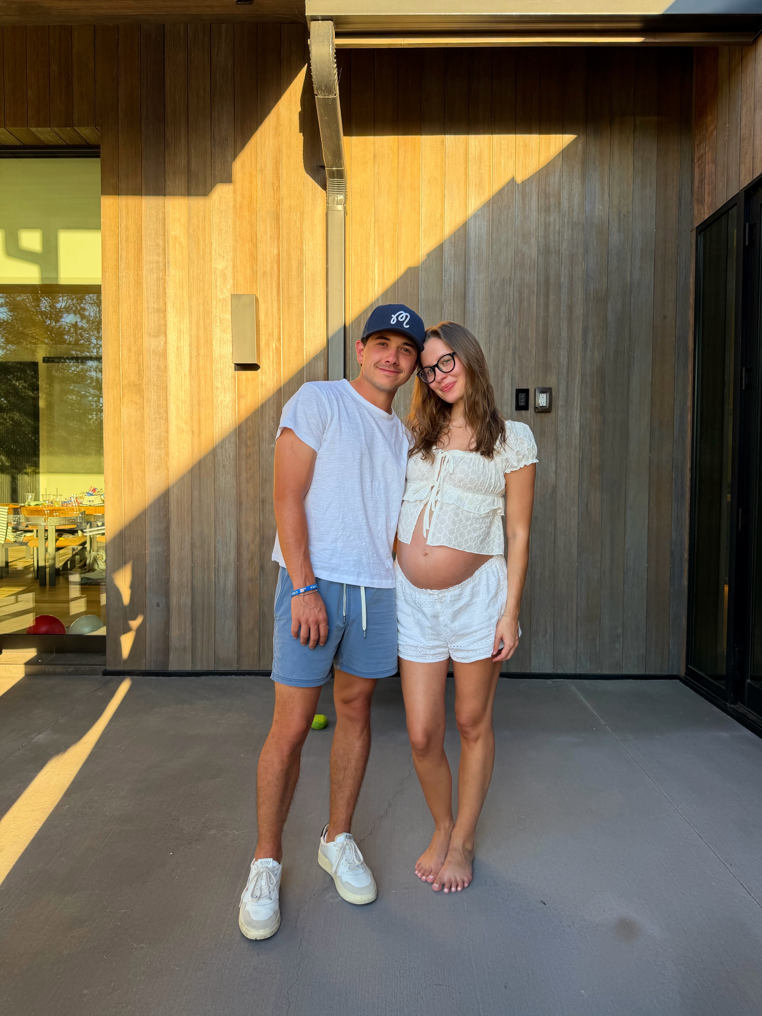 Bradley Perry and Natasha Bure Perry posing for a photo, with Natasha cradling her baby bump.