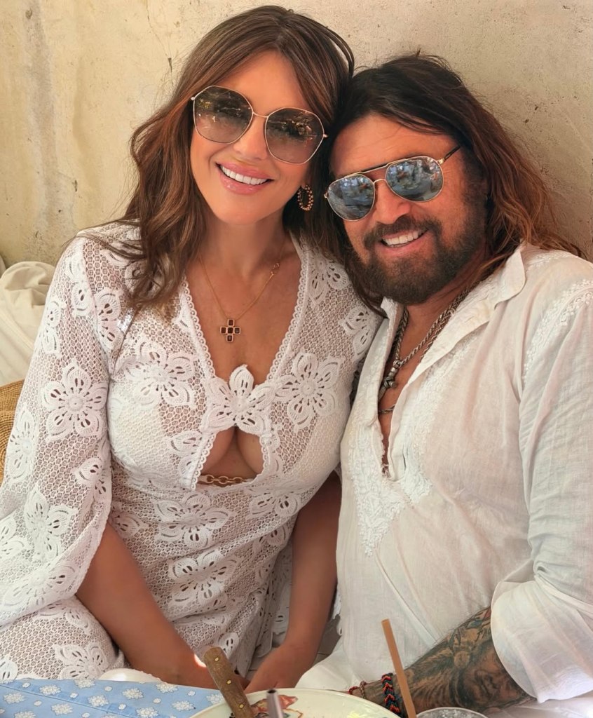 Elizabeth Hurley and Billy Ray Cyrus posing together while wearing white clothing and sunglasses.