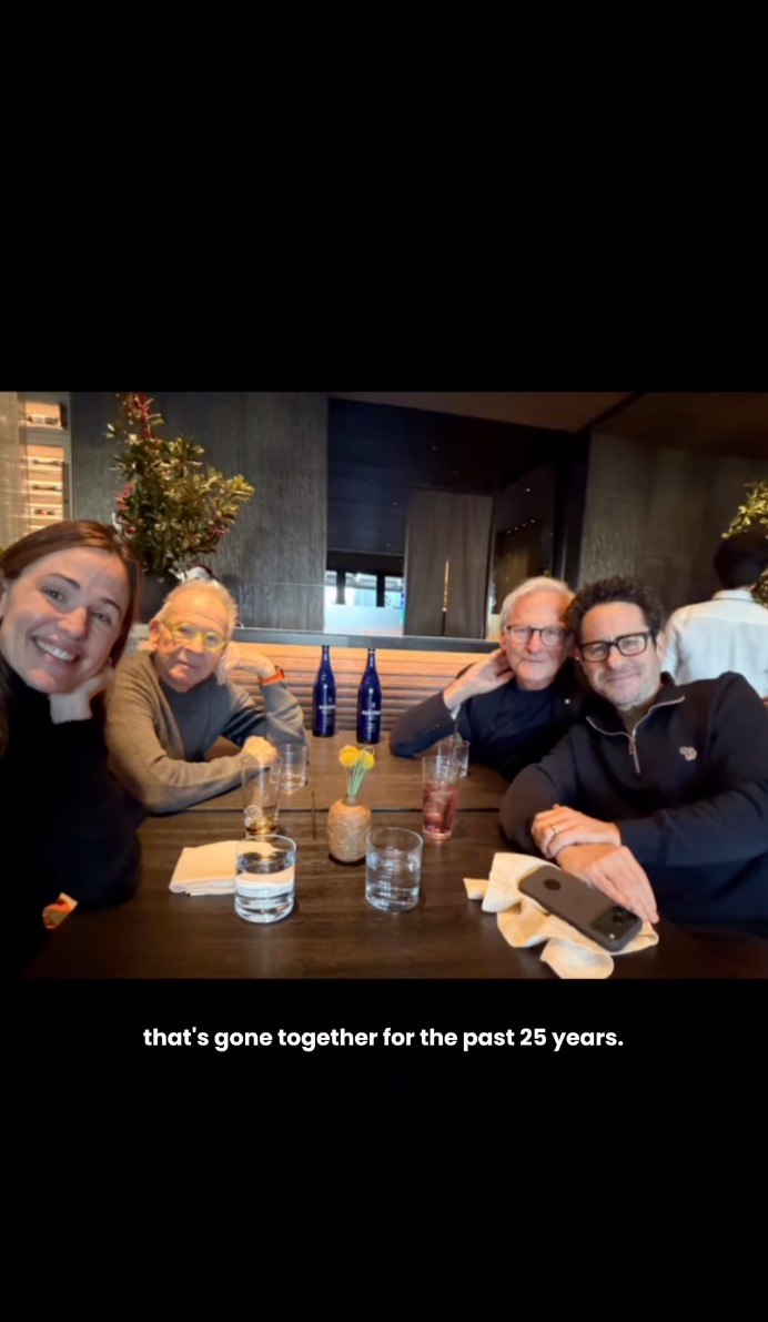 Jennifer Garner smiling while posing at a restaurant table with Alias cast and crew members.