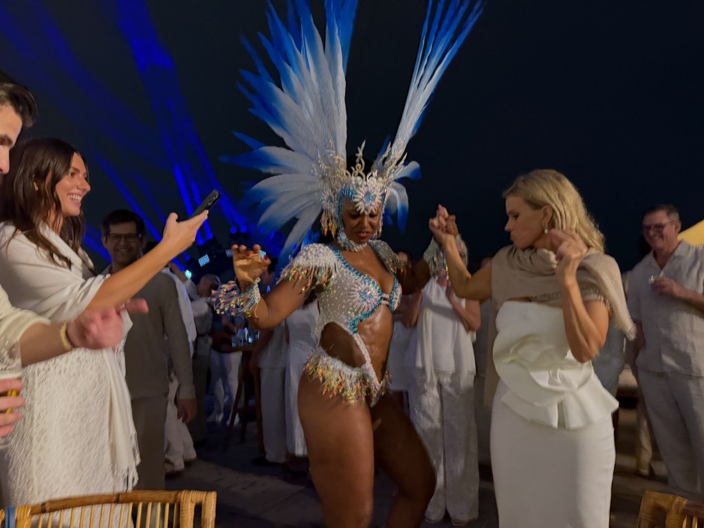 Guests dancing with a Brazilian performer in a feathered headdress at Conor Kennedy's wedding celebration.
