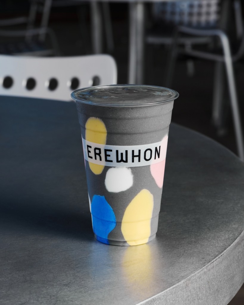 An Erewhon smoothie in a black cup with colorful spots on a table.