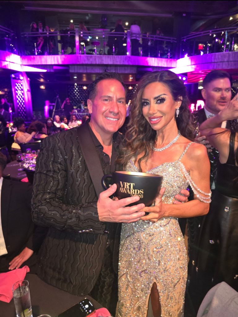 Rulla Nehme Pontarelli and Dr. Brian Pontarelli holding a VRT Awards 2026 trophy in a dimly lit, purple-hued venue.
