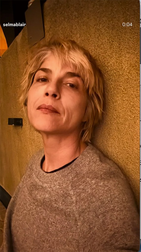 Selma Blair leaning against a textured wall while wearing a gray sweater.