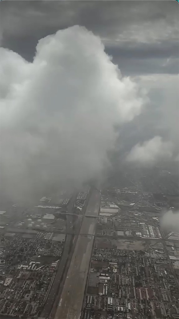 An aerial view from a plane of a city with a large cloud towering above it.