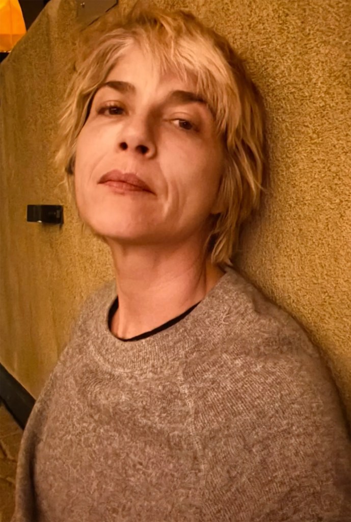 Selma Blair leaning against a textured wall while wearing a gray sweater.