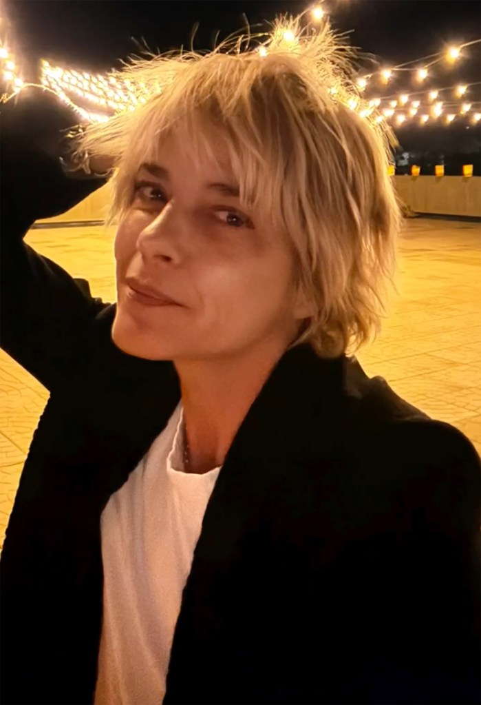 Selma Blair wearing a black jacket and white t-shirt, with string lights in the background.