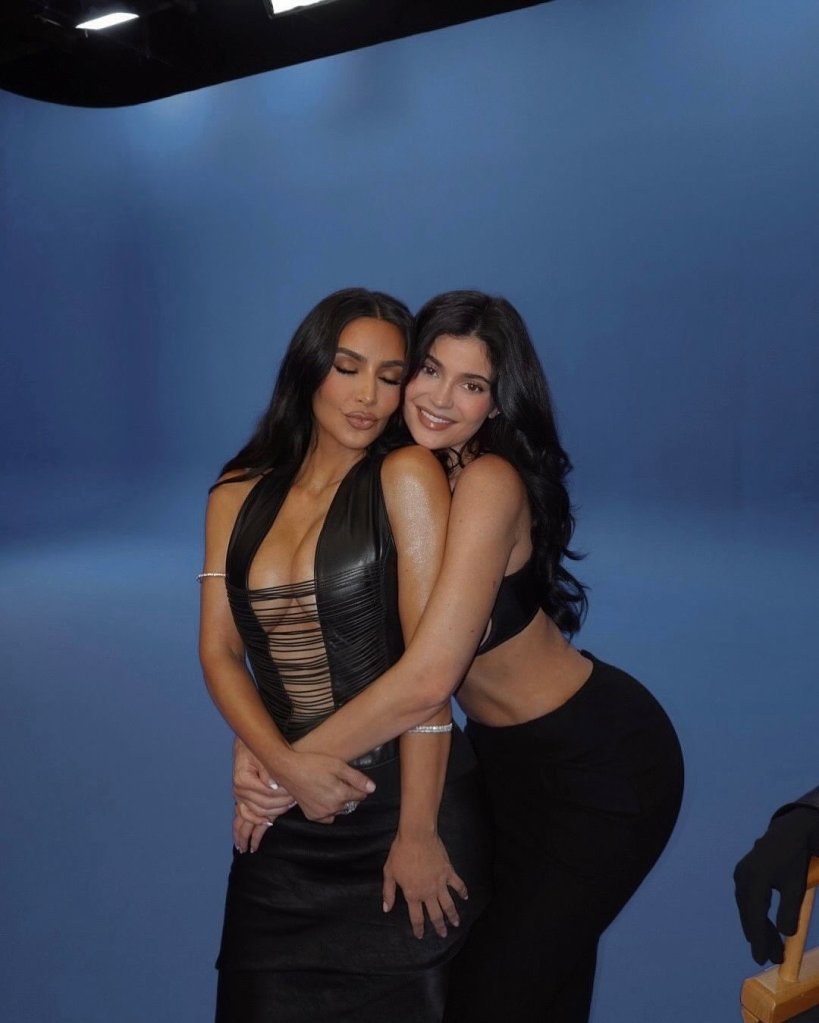 Kim Kardashian and Kylie Jenner pose together in a studio with a blue backdrop.