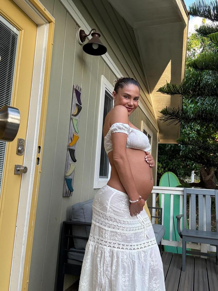 Model Sahara Ray poses outside on a porch, cradling her pregnant belly.