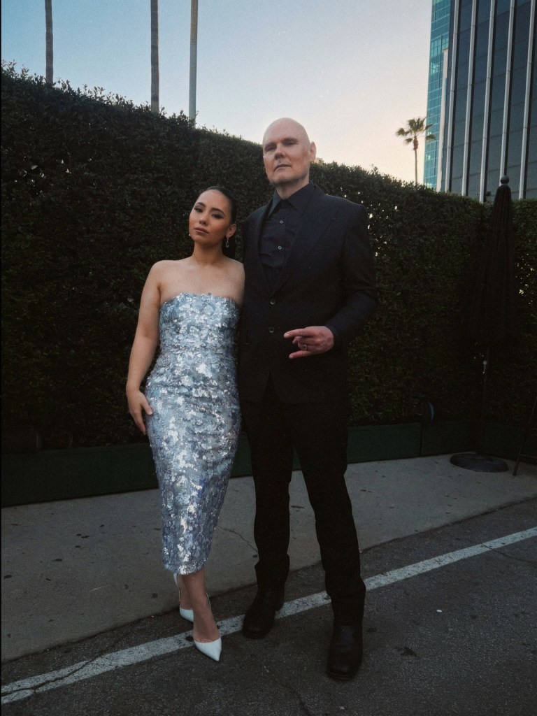 Billy Corgan and his wife, Chloe Mendel, pose together outdoors.