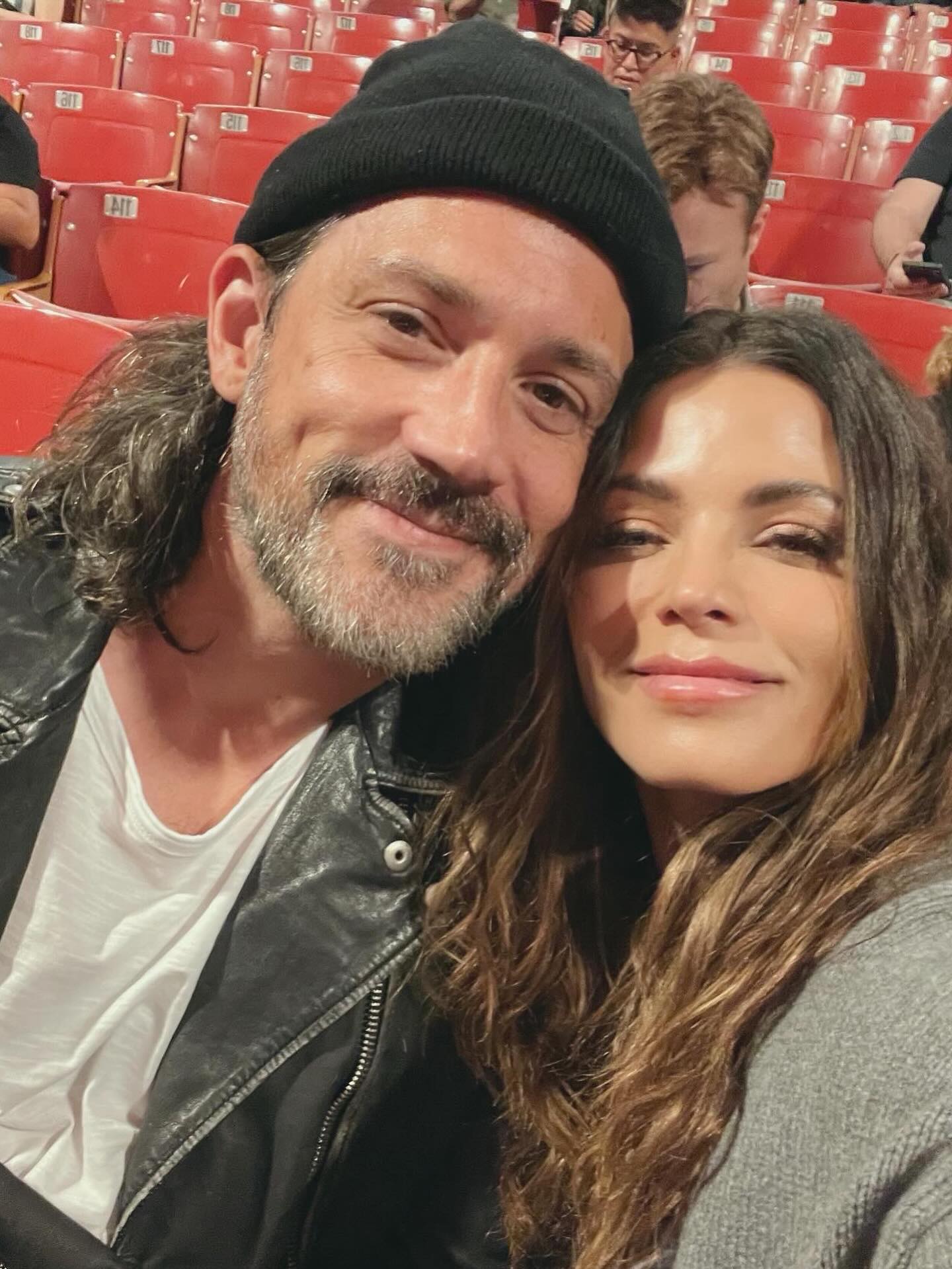 Steve Kazee and Jenna Dewan pose for a selfie in an auditorium with red seats.