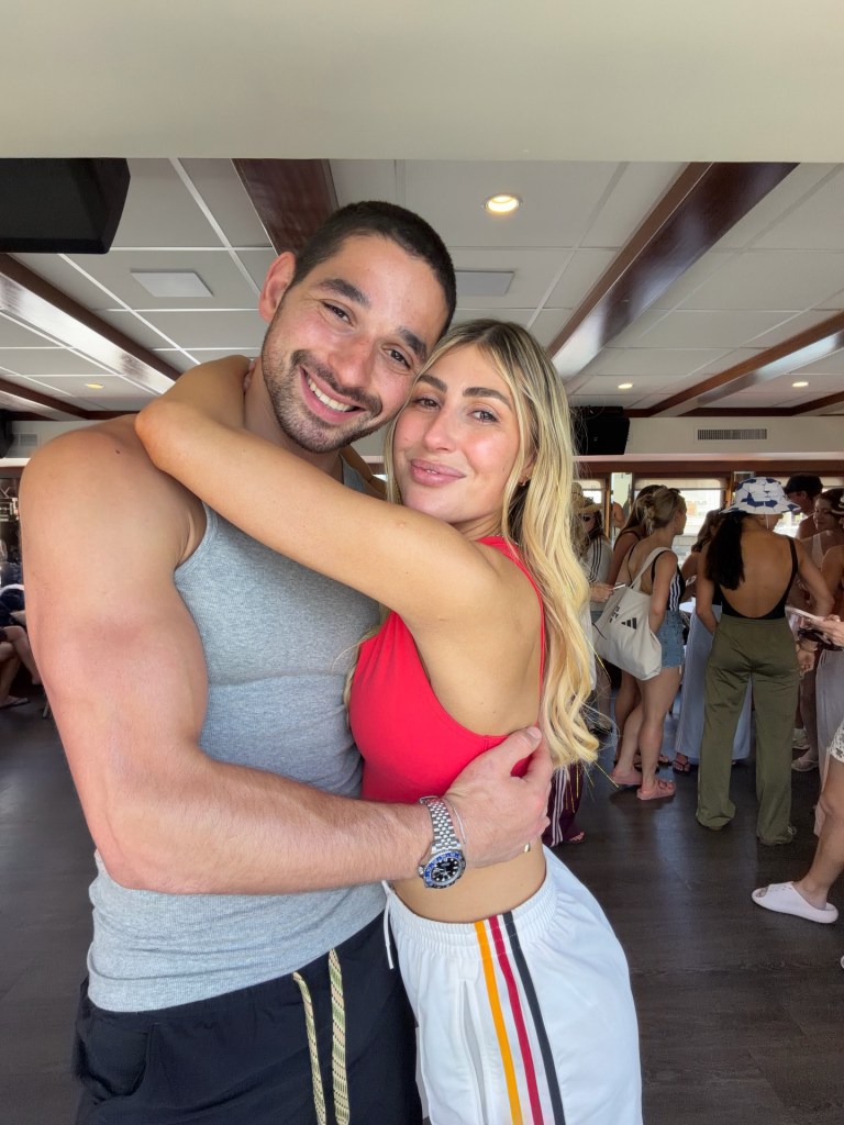 Emma Slater and Alan Bersten embracing inside a building with other people in the background.