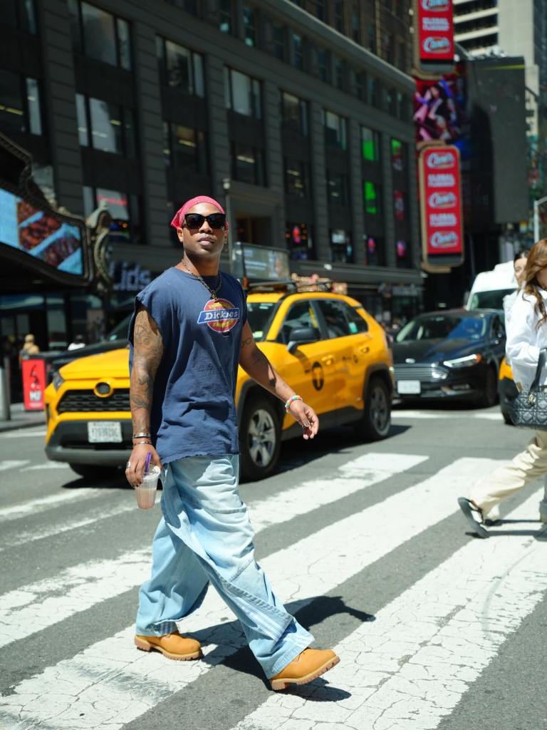 Todrick Hall wearing a blue sleeveless Dickies shirt, light wash jeans, and a red bandana while walking across a New York City street.