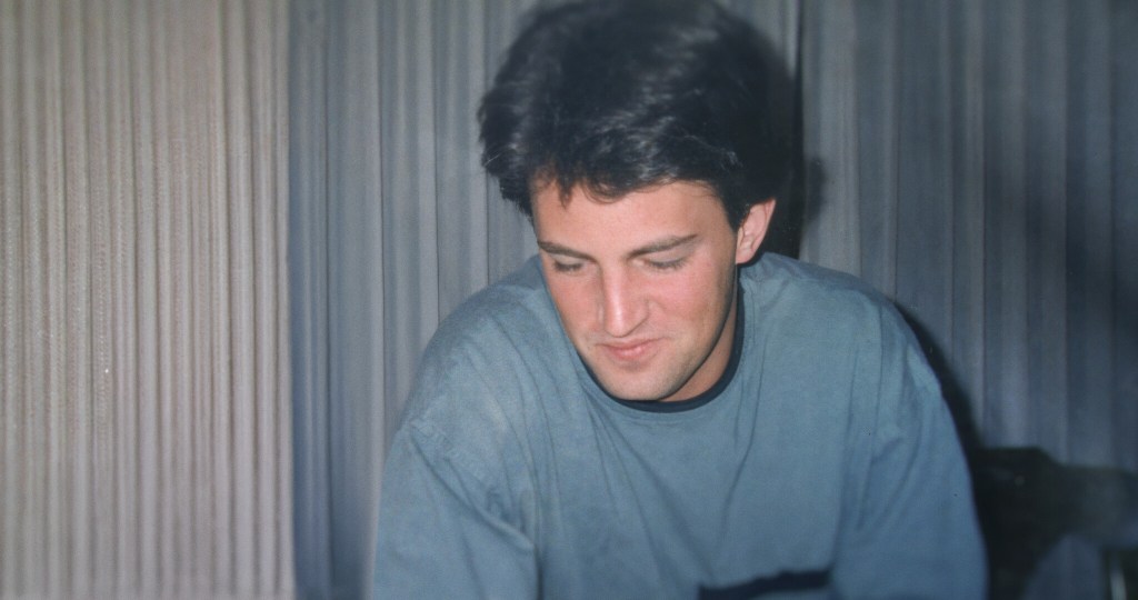 Matthew Perry in a blue shirt looking down.