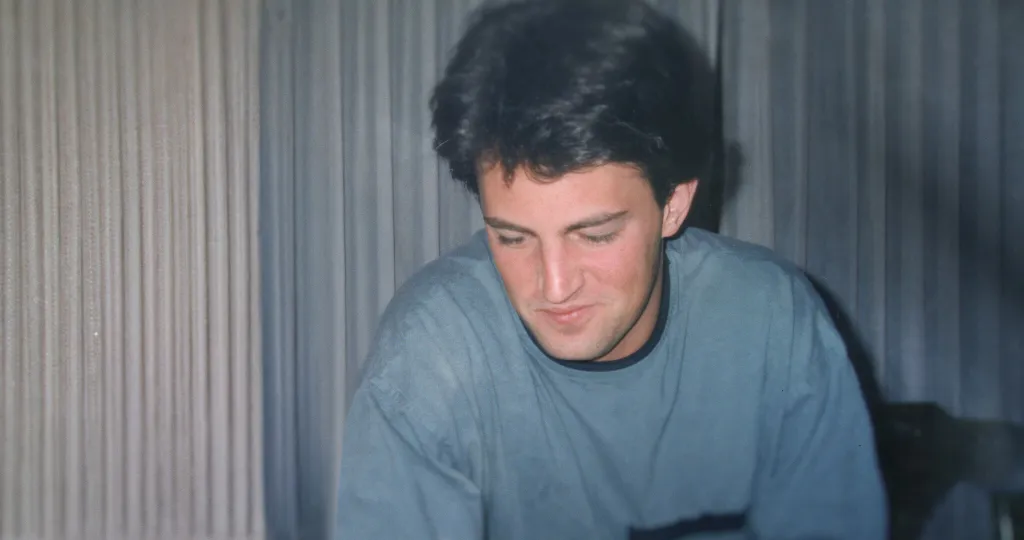 Matthew Perry looking down in a blue shirt.