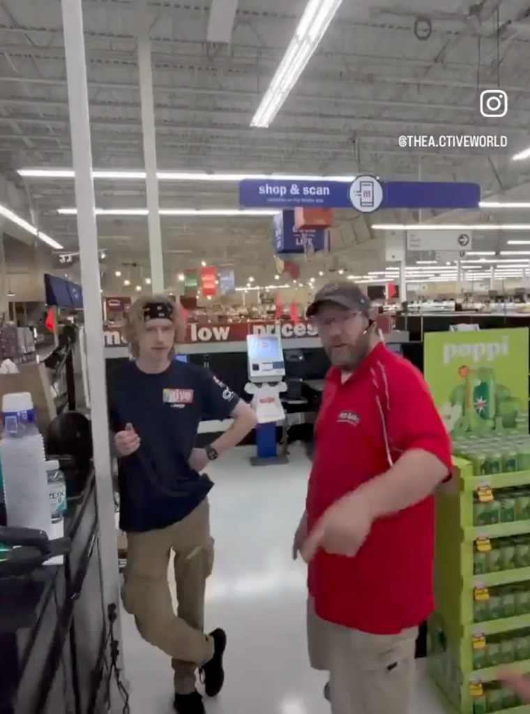 A young man in a dark t-shirt and a middle-aged man in a red polo shirt stand inside a grocery store.
