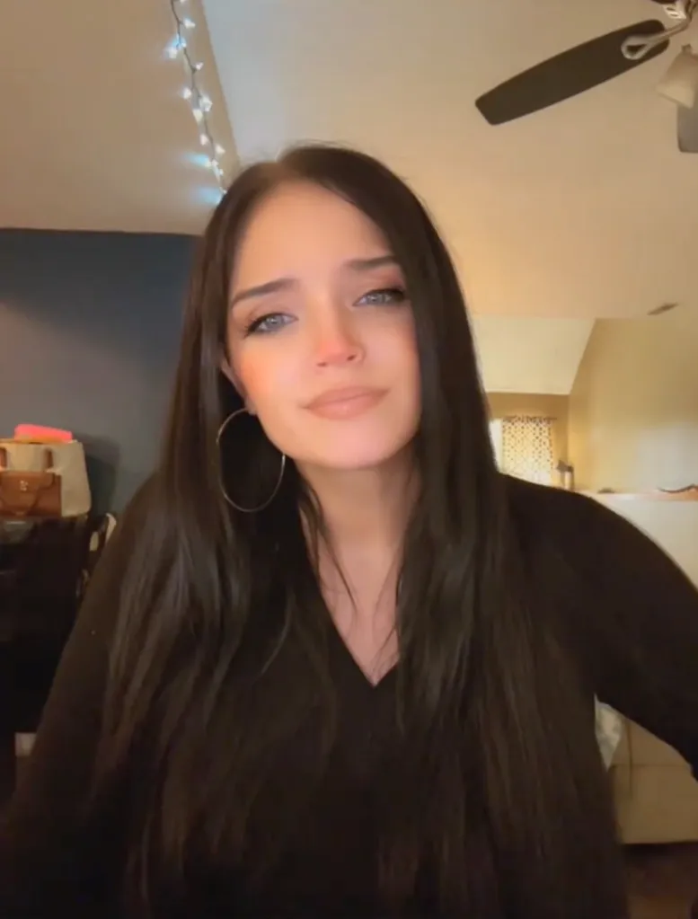 Autum Urker with long dark hair and hoop earrings, wearing a black top indoors.