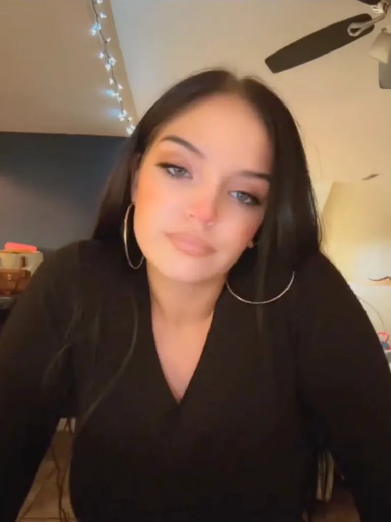 Autum Urker, wearing a black shirt and hoop earrings, looks towards the camera.