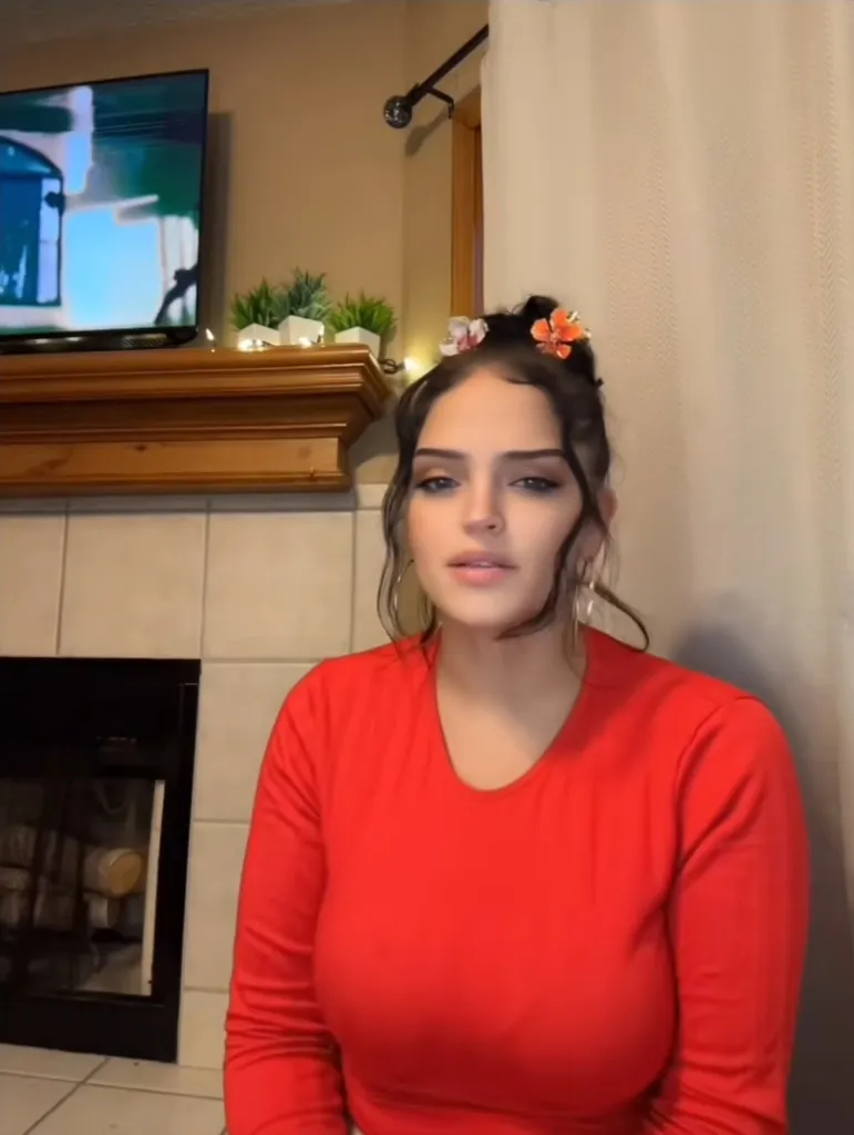 Autumn Urker wearing a red shirt with hair up in a bun in front of a fireplace.