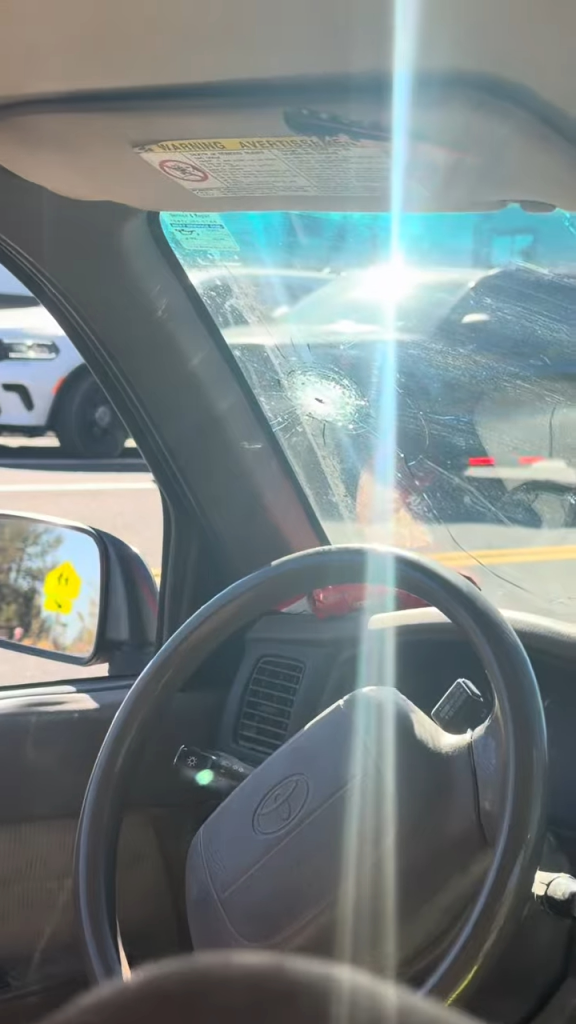 Interior view of a car showing a bullet hole and cracks in the front windshield.