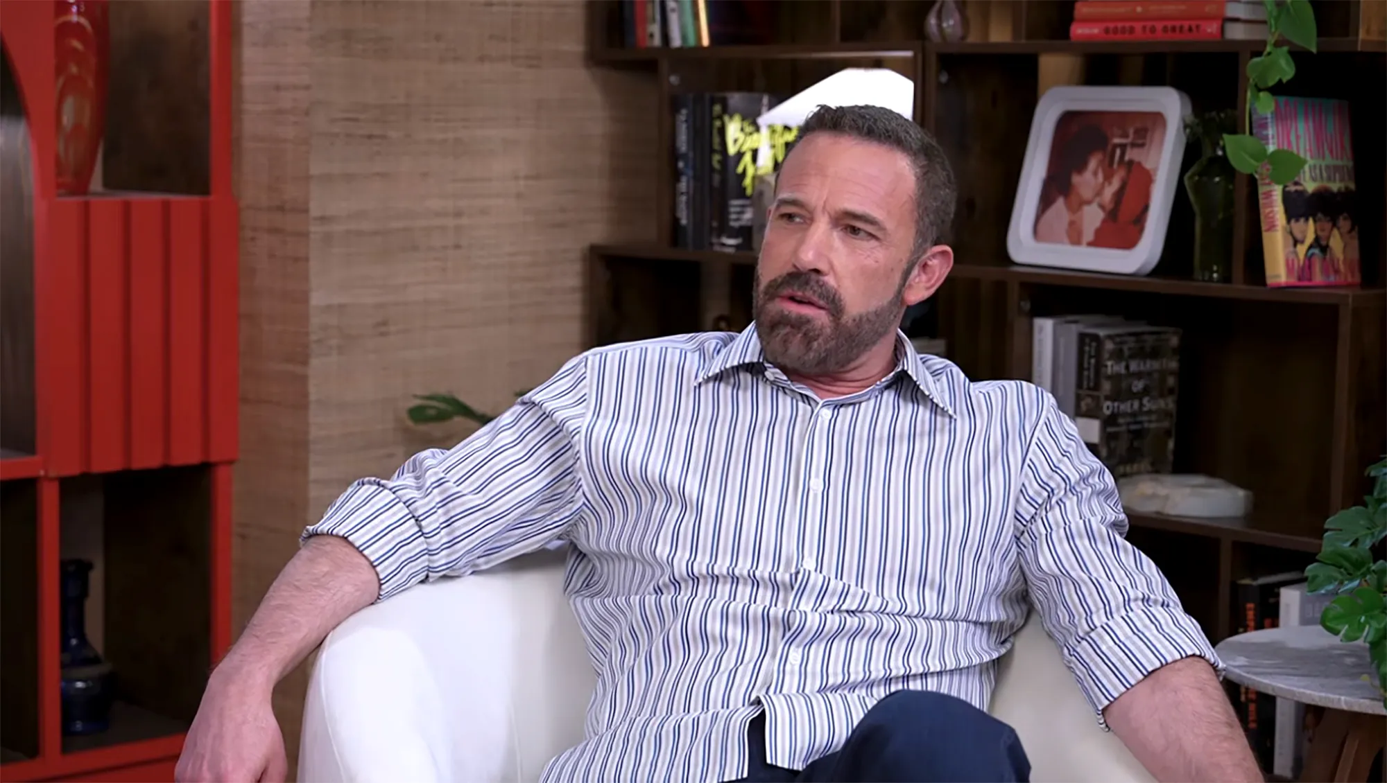 Ben Affleck sitting in a white armchair and speaking in an interview.