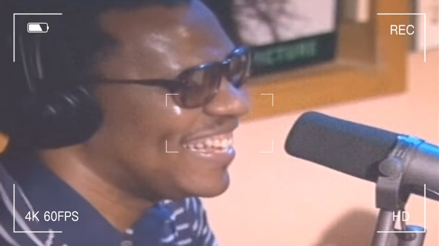 Ronnie Benjamin, also known as Big Black, wearing sunglasses and headphones while speaking into a microphone.