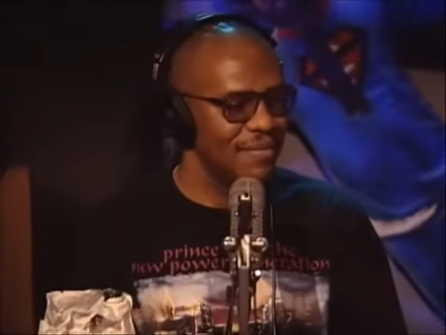 Ronnie Benjamin, also known as Big Black, wearing glasses and headphones while speaking into a microphone.