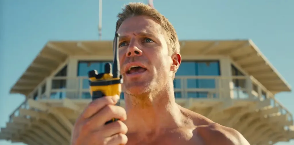 A lifeguard holding a walkie-talkie in front of a lifeguard tower.
