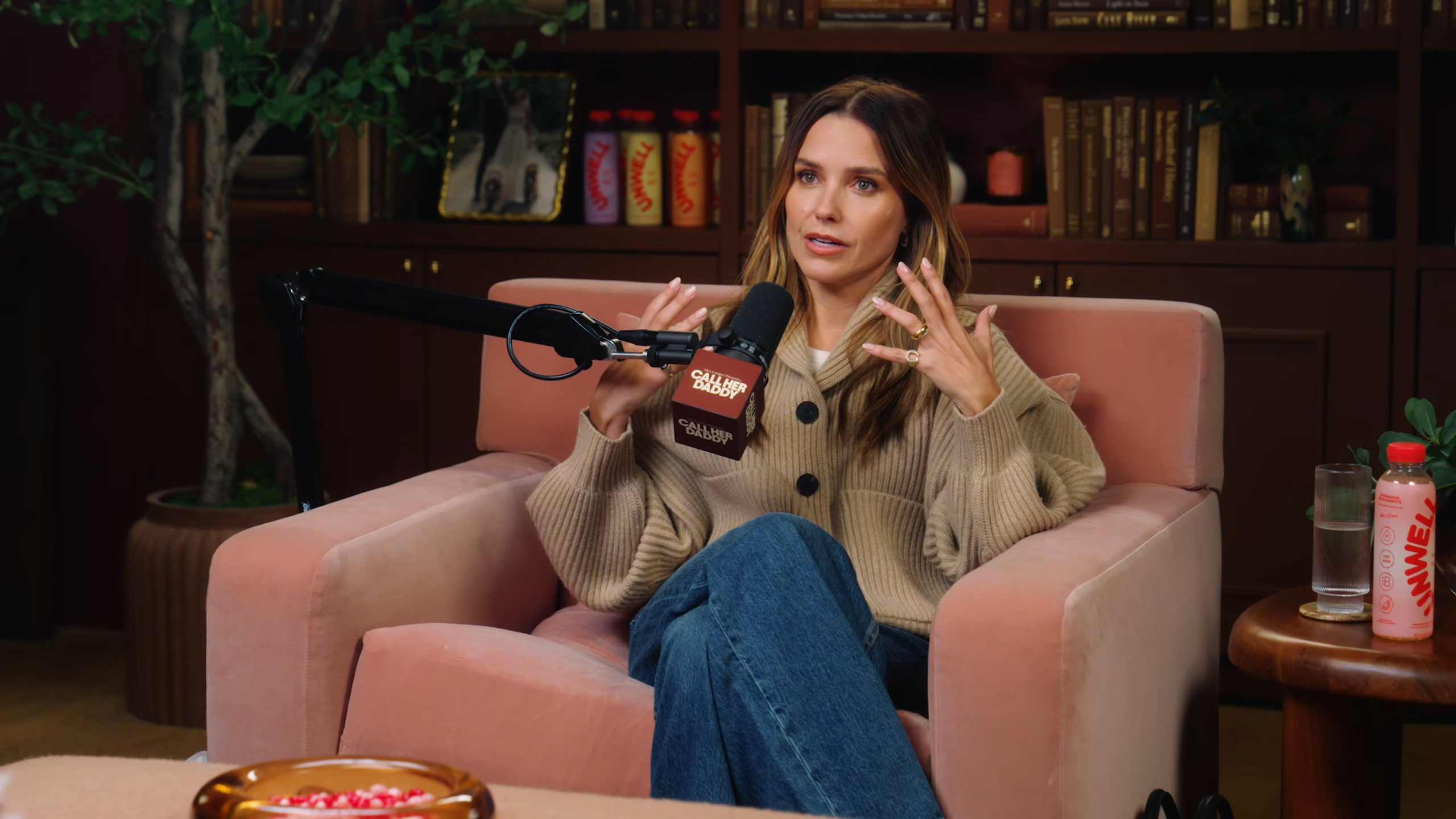 Sophia Bush sits in a pink armchair on the Call Her Daddy podcast, gesturing while speaking into a microphone.