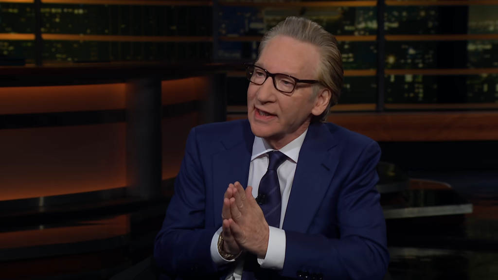 Bill Maher in a blue suit with his hands clasped during an interview.