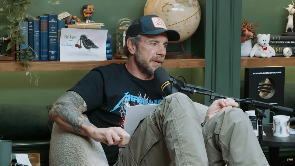 Dax Shepard sitting in a chair, speaking into a microphone.