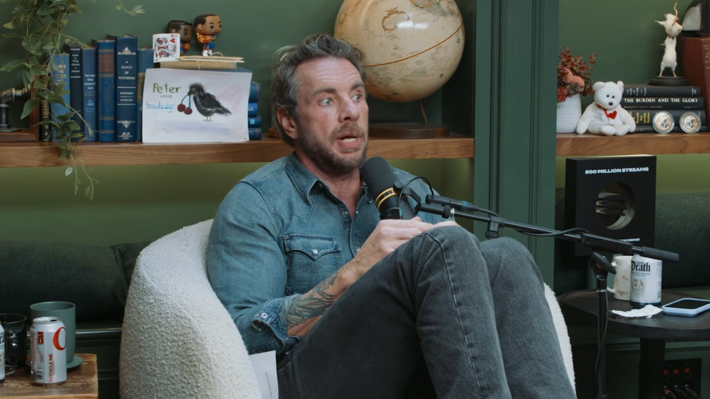 Dax Shepard sits in an armchair talking into a microphone on the Armchair Expert with Dax Shepard podcast.