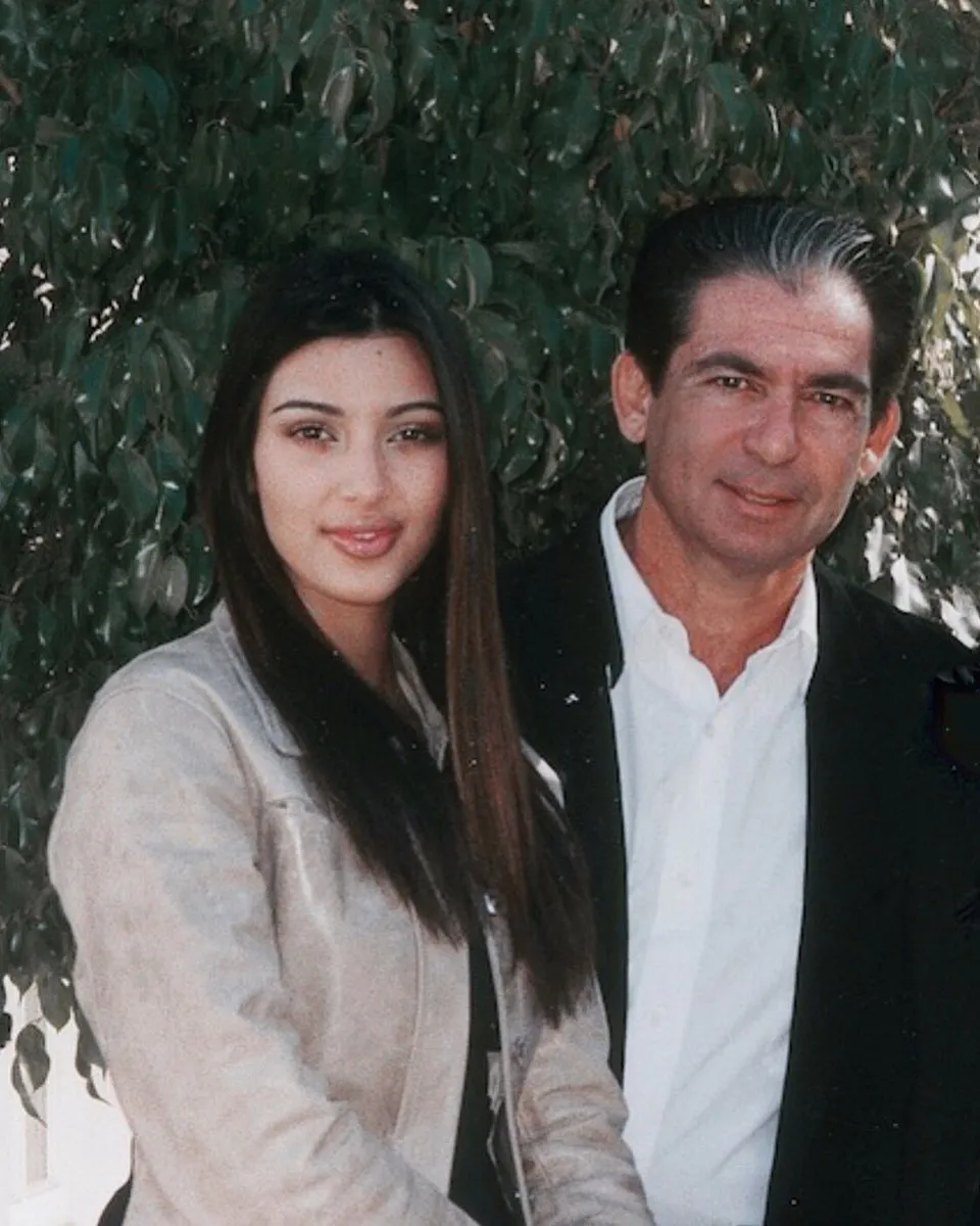 Kim Kardashian and her father, Robert Kardashian Sr., standing outdoors with foliage in the background.