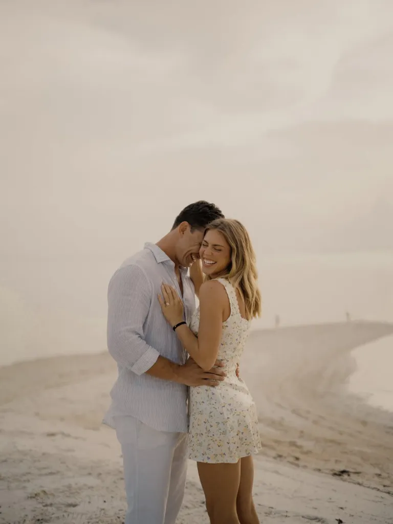 Tyler Cameron and his fiancée Tate Madden laughing and embracing on a beach.