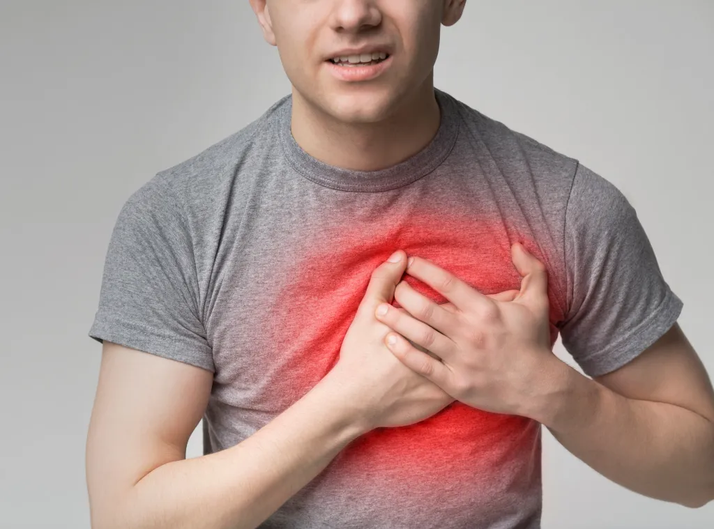 A young man holds his hands to his chest, experiencing chest pain with a red highlight indicating a heart attack.